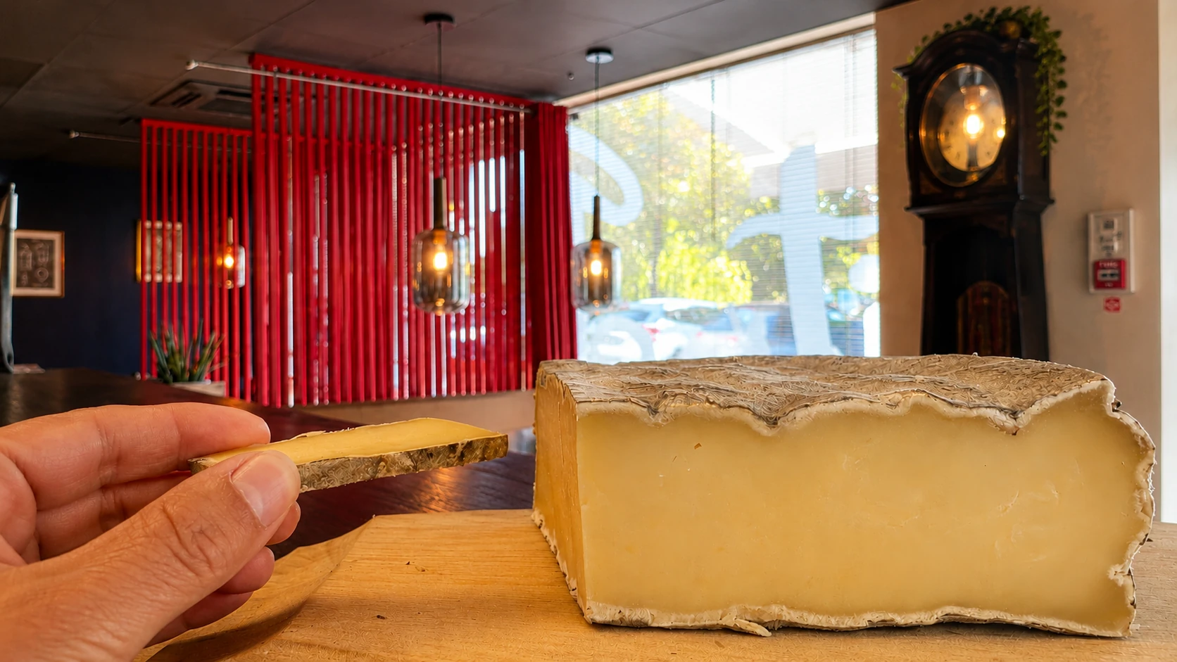 Morceau de croûte de Saint-Nectaire tenu entre les doigts devant un Saint-Nectaire au restaurant Let it Brie.